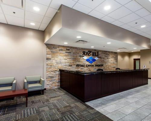 Reception area inside LeeSar Regional Service Center. Stone wall with LeeSar logo is behind a large u-shaped desk. Elevators and seating are on either side of the desk.